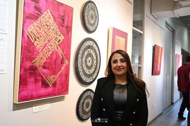 Hala Ali with the magenta gold-calligraphy painting at exhibition